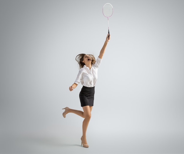 Mujer caucásica en ropa de oficina juega bádminton aislado en la pared gris