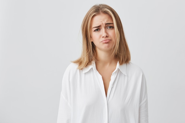 Mujer caucásica rubia que parece infeliz e insatisfecha, frunciendo el ceño, mirando tristemente. Hermosa chica con pelo rubio posando. Concepto de personas y emociones.