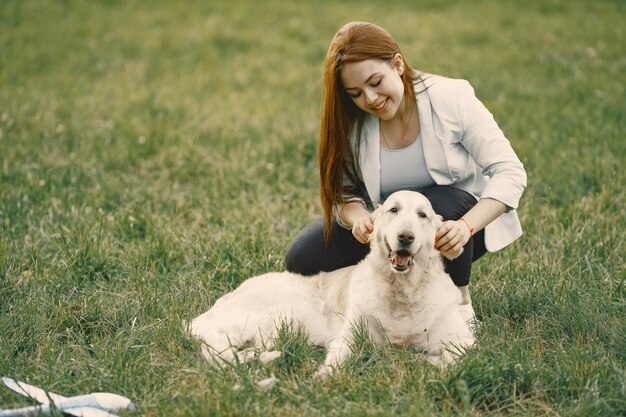 Mujer caucásica sentada sobre un césped con su perro. Chica vestida de jeans y chaqueta blanca
