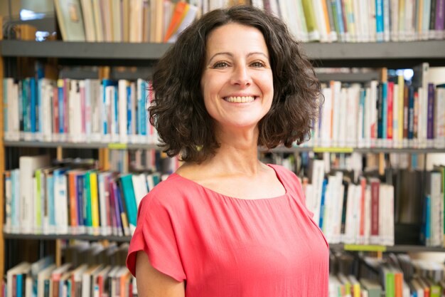 Mujer caucásica sonriente que presenta en la biblioteca pública