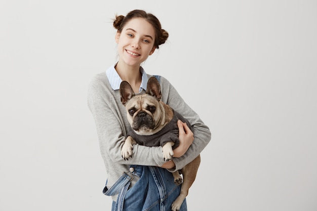 Foto gratuita mujer caucásica y su adorable mascota con sonrisa. fotógrafo de sexo femenino alegre que toma la imagen de ella y del perro de pedigrí que miente en sus manos. concepto de amistad