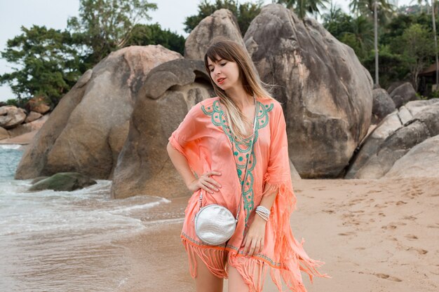 mujer caucásica en vestido boho de verano tropical caminando por la playa.