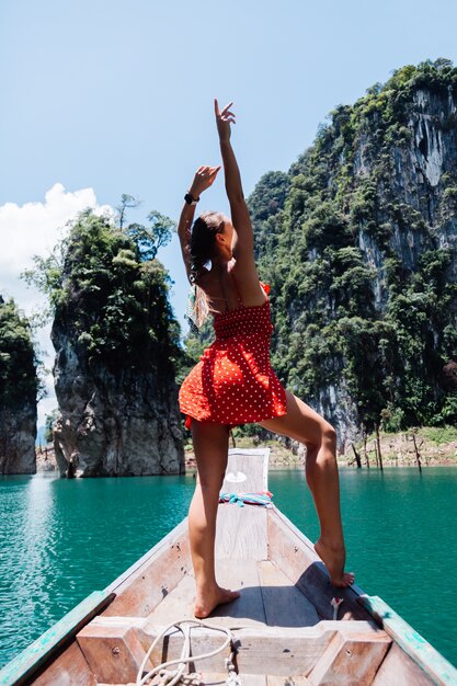 Mujer caucásica en vestido rojo de verano en barco asiático tailandés de vacaciones, viajar por Tailandia