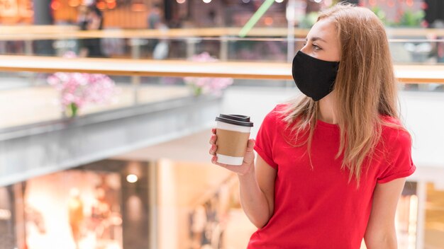 Mujer en el centro comercial con máscara y taza de café