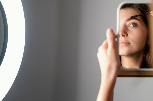 Mujer cepillándose las cejas mientras se mira en el espejo después del tratamiento con espacio de copia