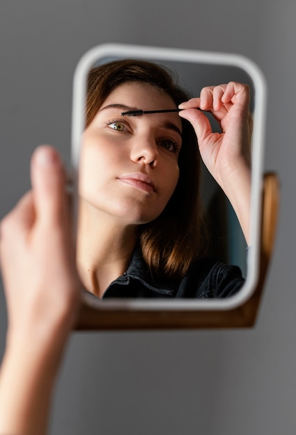 Mujer cepillándose las cejas mientras se mira en el espejo después del tratamiento