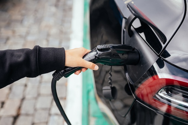 Mujer cerca de coche eléctrico. Vehículo cargado en la estación de carga.