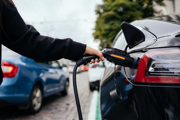 Mujer cerca de coche eléctrico. Vehículo cargado en la estación de carga.