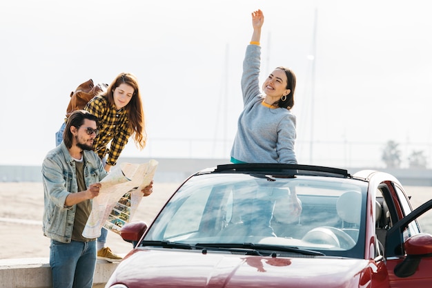 Mujer cerca del hombre que mira el mapa y dama positiva que se inclina hacia fuera del coche