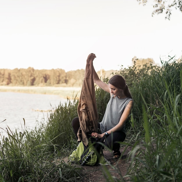 Foto gratuita mujer cerca del lago, quitando la sudadera de la bolsa