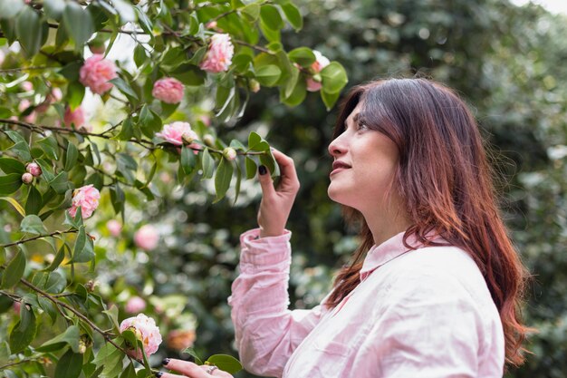 Mujer cerca de muchas flores rosadas que crecen en ramitas verdes