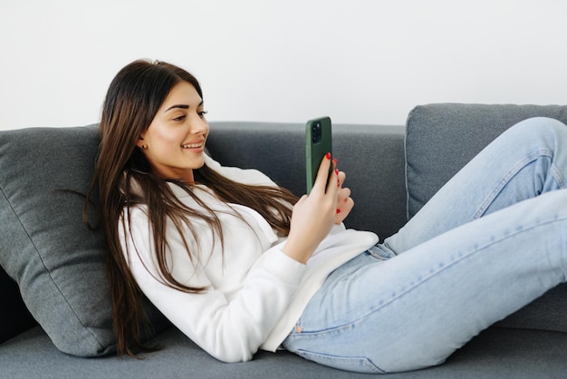 Mujer de cerca sentada en el sofá sosteniendo un teléfono inteligente en casa