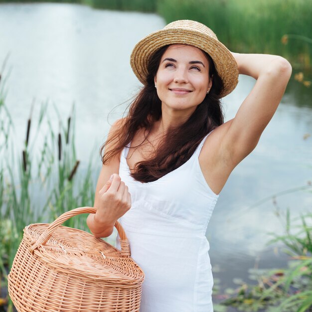 Mujer con cesta de picnic posando junto al lago