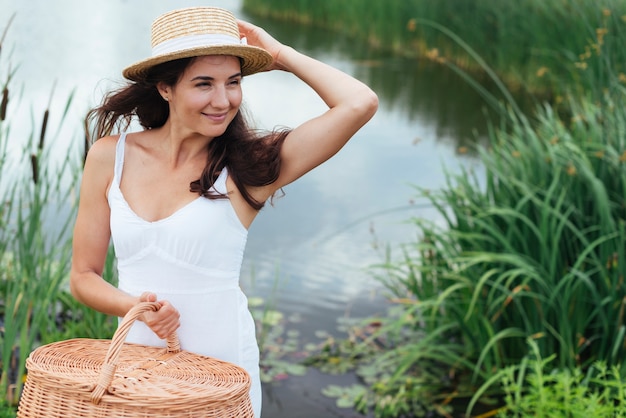 Mujer con cesta de picnic posando junto al lago