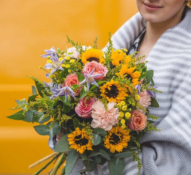 Mujer con chal sosteniendo un ramo de flores en fondo amarillo