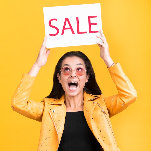 Mujer de chaqueta amarilla sosteniendo un banner de venta plano medio