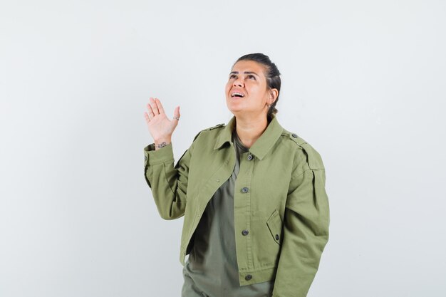 Mujer con chaqueta, camiseta agitando la mano mientras mira hacia arriba y parece esperanzada