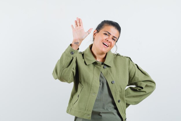 Mujer con chaqueta, camiseta agitando la mano para saludar y lucir alegre