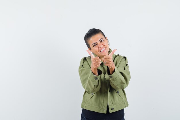 Mujer en chaqueta, camiseta mostrando doble pulgar hacia arriba y mirando confiada