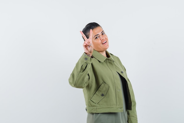 Mujer en chaqueta, camiseta mostrando gesto de victoria y mirando confiado