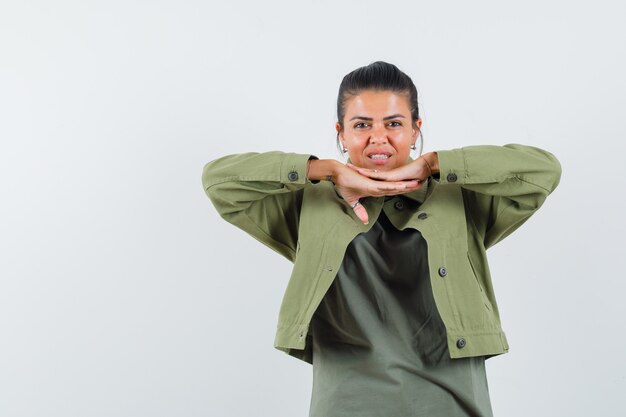 mujer en chaqueta, camiseta tomados de la mano debajo de la barbilla y luciendo linda