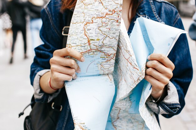 La mujer en chaqueta de los pantalones vaqueros se sostiene en su mapa turístico de las manos
