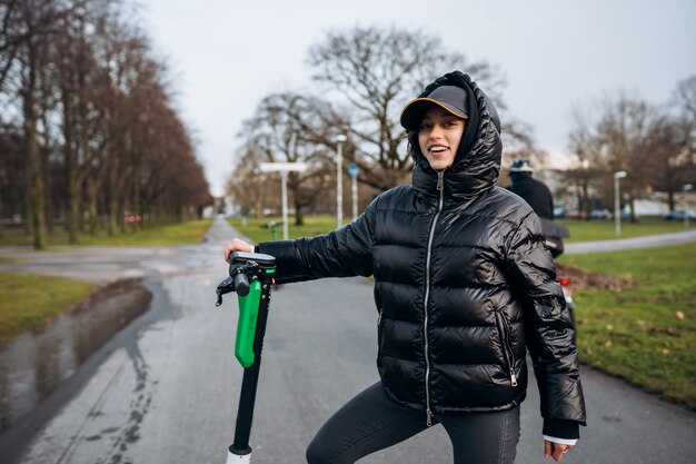 Mujer en una chaqueta en un scooter eléctrico en un parque de otoño