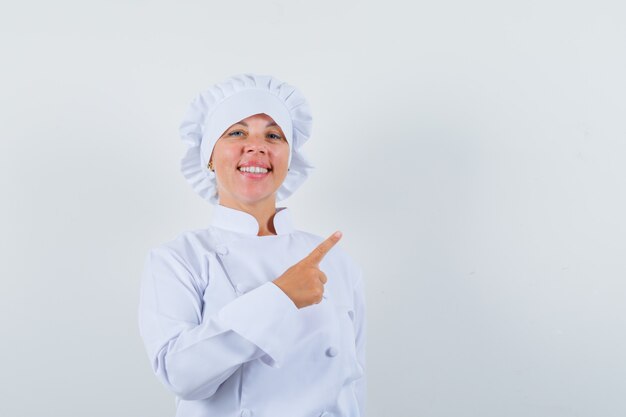 Mujer chef apuntando a la esquina superior derecha con uniforme blanco y mirando confiado