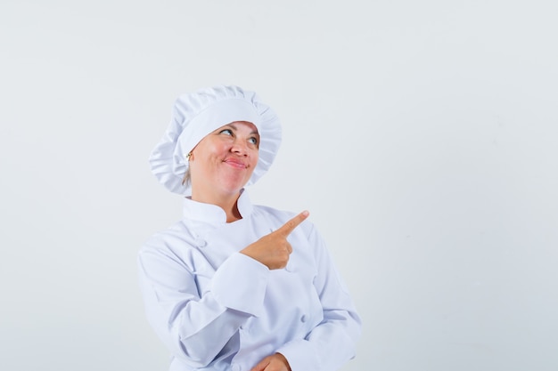 Mujer chef apuntando a la esquina superior derecha con uniforme blanco y mirando vacilante