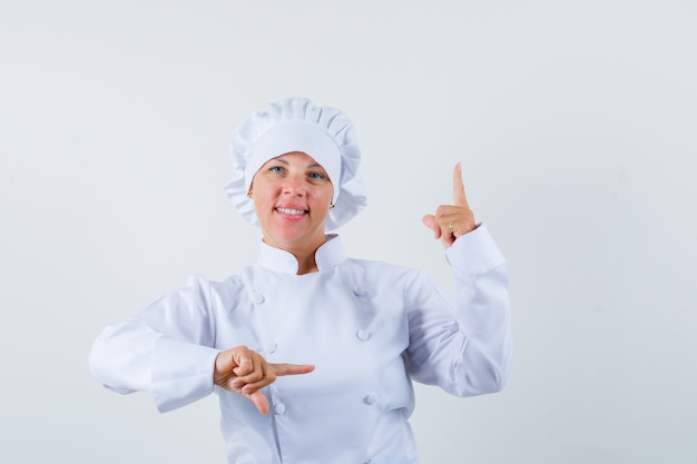 mujer chef apuntando a un lado y hacia arriba con uniforme blanco y mirando confiada.