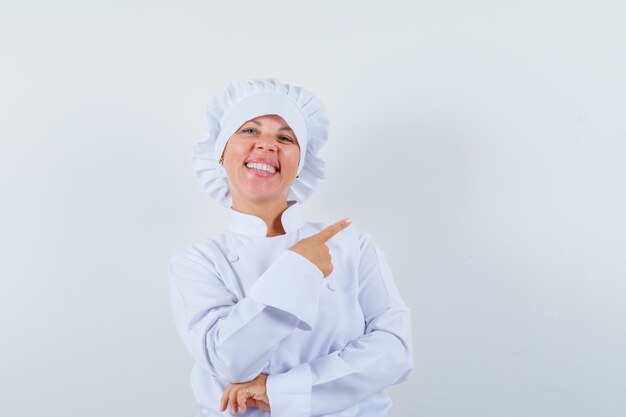 mujer chef apuntando hacia el lado derecho con uniforme blanco y mirando contenta.