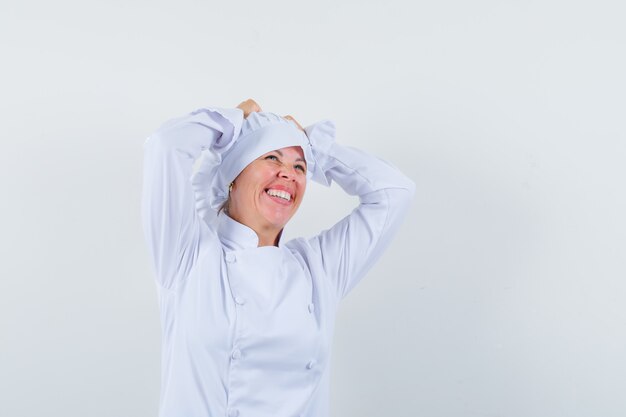 mujer chef cogidos de la mano en la cabeza con uniforme blanco y mirando dichosa.