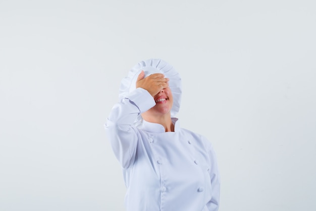 Mujer chef cubriendo los ojos con la mano en uniforme blanco y mirando alegre
