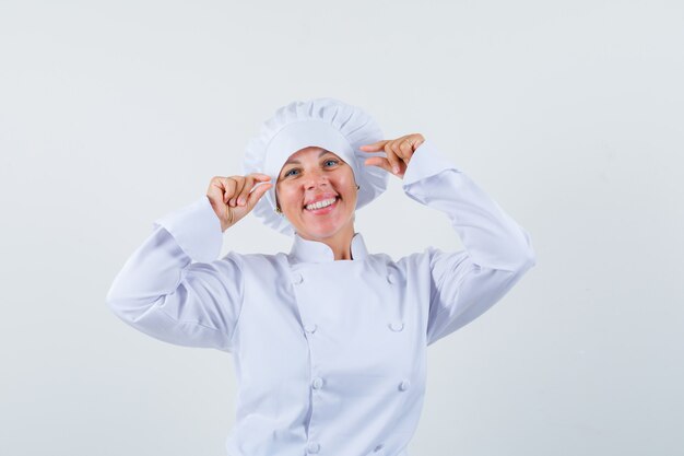 mujer chef mostrando un cartel de tamaño pequeño en uniforme blanco y con aspecto positivo.