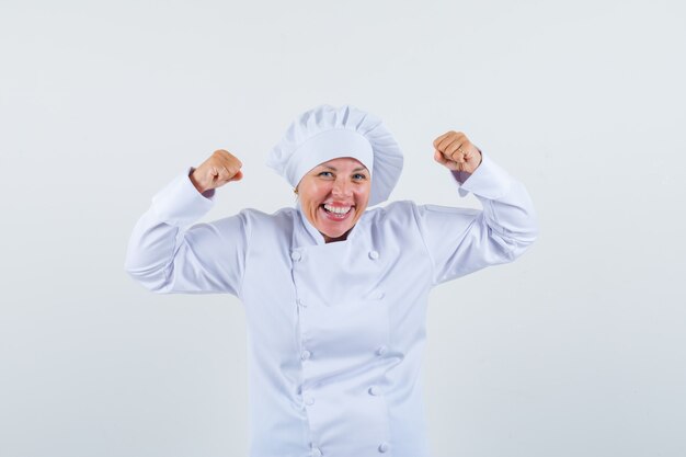 mujer chef mostrando gesto de ganador en uniforme blanco y mirando alegre.