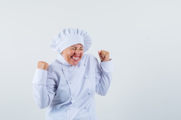 mujer chef mostrando gesto de ganador en uniforme blanco y mirando alegre.