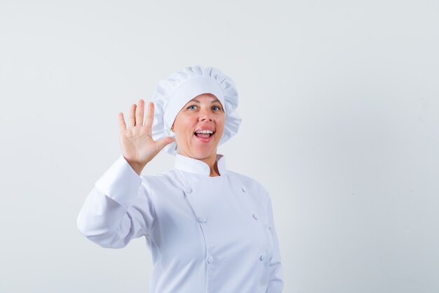 Mujer chef mostrando palm en uniforme blanco y mirando confiado