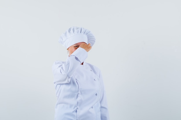 Mujer chef pellizcando su nariz en uniforme blanco y mirando preocupado