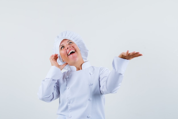 mujer chef posando como hablando por teléfono mientras extiende la palma a un lado en uniforme blanco y se ve habladora.