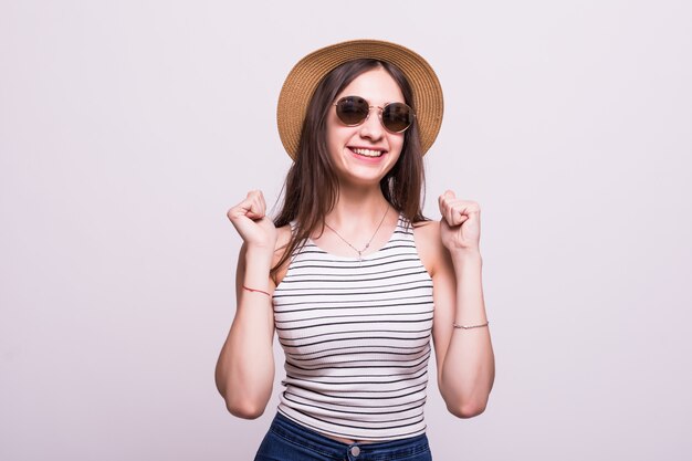 Mujer china con sombrero gafas de sol de pie sobre fondo blanco aislado celebrando sorprendido y asombrado por el éxito con los brazos levantados y los ojos abiertos. Concepto ganador.