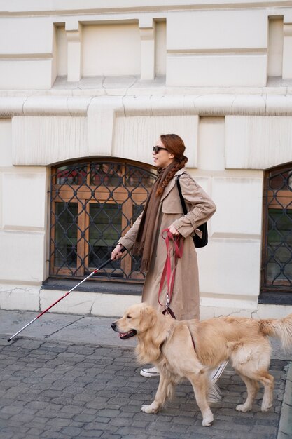 Mujer ciega sonriente de tiro completo con perro de servicio