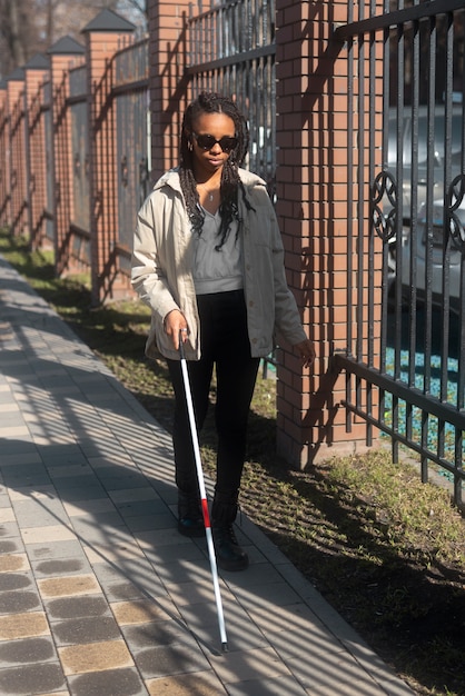 Mujer ciega de tiro completo caminando con bastón blanco