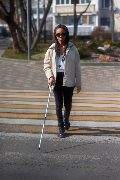 Mujer ciega de tiro completo en el cruce de peatones con bastón