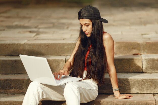 Mujer en una ciudad primaveral. Señora con una computadora portátil. Chica sentada en una escalera.