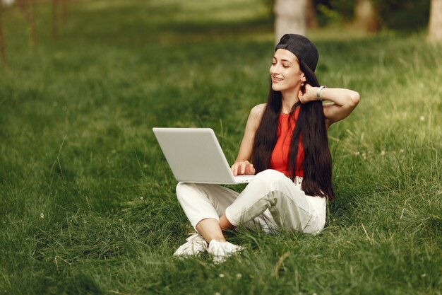 Mujer en una ciudad primaveral. Señora con una computadora portátil. Niña sentada sobre un césped.