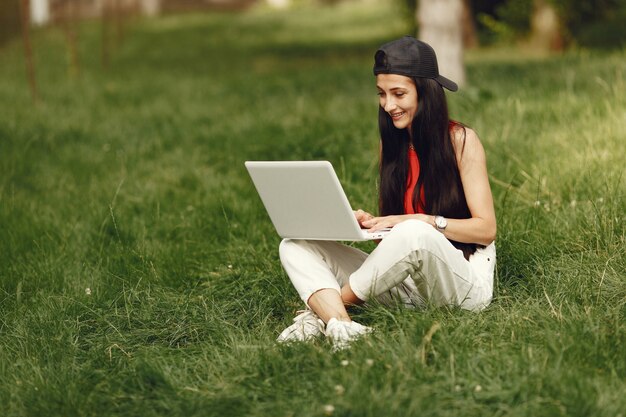 Mujer en una ciudad primaveral. Señora con una computadora portátil. Niña sentada sobre un césped.