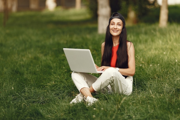 Mujer en una ciudad primaveral. Señora con una computadora portátil. Niña sentada sobre un césped.