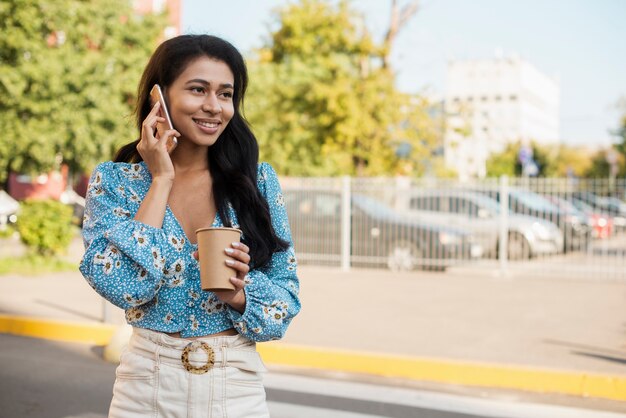 Mujer en la ciudad con teléfono y café.