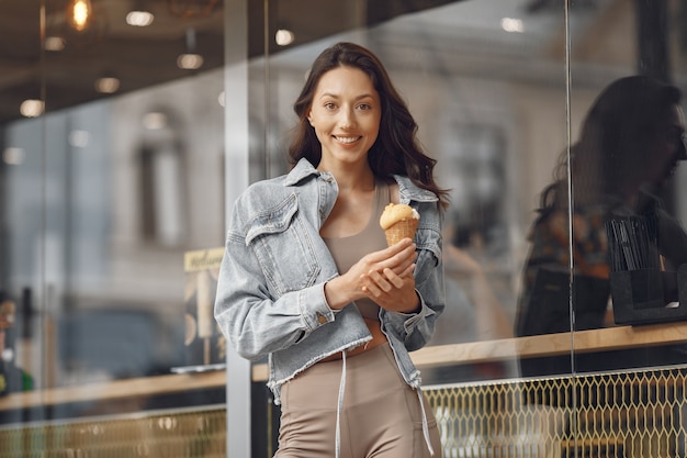 Mujer en una ciudad veraniega. Señora con helado. Morena por el edificio.