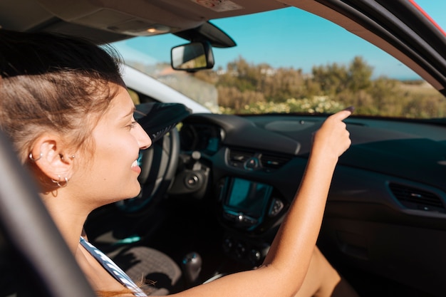 Mujer en coche sonriendo y mostrando la mano hacia adelante